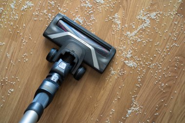 Elektrikli süpürge hortumu dağınık pirinç tanelerini ahşap zemin temizleme, dağınıklık ve ev bakımı konseptinden topluyor..