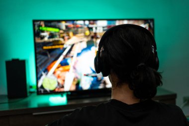 Kulaklık takan genç oyuncu konsolun arka planında oynuyor..