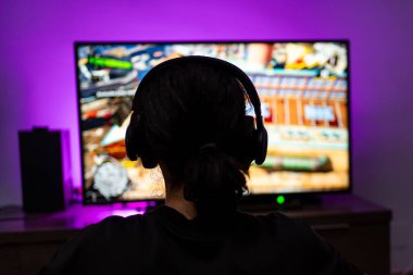 Kulaklık takan genç oyuncu konsolun arka planında oynuyor..