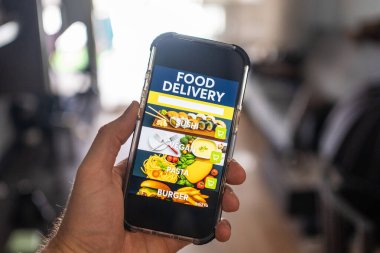 Ekranda yemek dağıtım uygulaması olan erkek el bilgisayarı evdeki odanın arka planına karşı