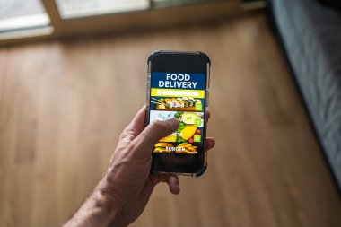 Ekranda yemek dağıtım uygulaması olan erkek el bilgisayarı evdeki odanın arka planına karşı