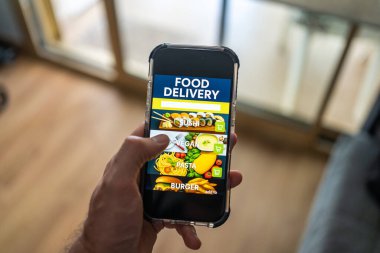 Ekranda yemek dağıtım uygulaması olan erkek el bilgisayarı evdeki odanın arka planına karşı