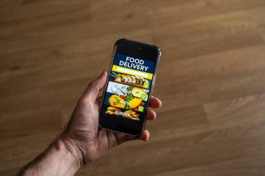 Ekranda yemek dağıtım uygulaması olan erkek el bilgisayarı evdeki odanın arka planına karşı