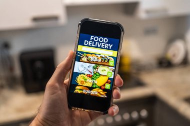 Ekranda yemek dağıtım uygulaması olan erkek el bilgisayarı evdeki odanın arka planına karşı