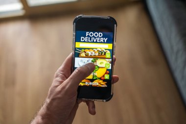 Ekranda yemek dağıtım uygulaması olan erkek el bilgisayarı evdeki odanın arka planına karşı