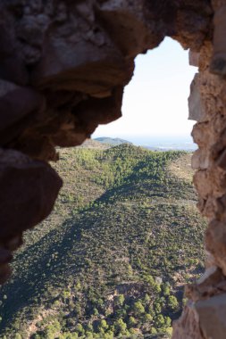 Dağlık yeşil bitki örtüsüyle kaplı, etkileyici bir manzara. Bir kaya oluşumundaki doğal bir açıklıktan çekildi. Görüntü doğal elementleri eşsiz bir çerçeve ile birleştiriyor, doğanın güzelliğini beklenmedik bir şekilde gösteriyor.