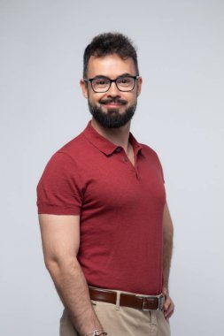 Kırmızı polo tişörtlü, kameraya bakarken nazikçe gülümseyen güçlü, arkadaş canlısı bir adamın portresi. Temiz beyaz bir arkaplanda çekilen görüntü güven, profesyonellik ve samimiyeti çağrıştırıyor. İş, yaşam tarzı veya sağlıkla ilgili içerik için ideal.