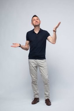 Güçlü, kendine güvenen, siyah polo giymiş, kolları açık ve avuçları yukarı bakan, gökyüzüne bakan beyaz bir adamın bütün vücut portresi. Temiz beyaz bir arkaplan karşısında, bu güçlü ve sembolik duruş içgözlem gösterir.