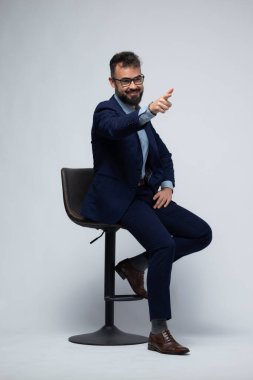 Mavi takım elbiseli bir İspanyol 'un tabureye oturmuş, ileriye bakarken kendinden emin bir şekilde yan tarafı işaret edişi. Mesajlaşma temaları, eylem çağrısı kampanyaları, sunumlar ve iş dünyasına uyan dinamik ve direktif bir jest