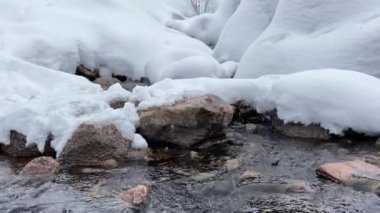 Bir dağ deresinin suyu taşların ve karın arasında ses ile akıyor.