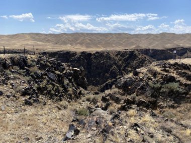 Siyah kanyon ve siyah kayalar. Arka planda bulutlar olan mavi bir gökyüzü şeridi