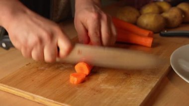Tahta kesme tahtasının üzerinde mutfak bıçağıyla havuç doğramak.