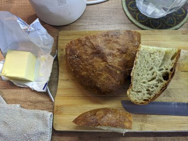 Fotoğraf sergileri, ahşap bir tahtanın üzerinde taze kesilmiş ev yapımı ekşi ekmek dilimleri, yanına bir bıçak yerleştirilmiş ve yayılmak üzere olan bir parça tereyağı. Ekmeğin kırsal görünümü, altın kabuğu ve yumuşak iç yüzüyle