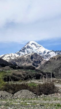 Kazbek Dağı 'nın karla kaplı zirvesinin göz kamaştırıcı manzarası, etrafındaki engebeli araziden görkemli bir şekilde yükseliyor. Kış havası ve el değmemiş beyaz yamaçlar büyüleyici bir doğal güzellik manzarası yaratır.
