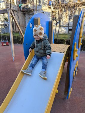 Neşeli iki yaşındaki bir çocuk, renkli fil şekilli bir kaydırağın üzerinden neşeli bir çocuk oyun parkında kayıyor. Slaytın canlı tasarımı oyun alanına eğlenceli ve yaratıcı bir dokunuş ekleyerek genç çocuklar için güvenli ve heyecan verici bir deneyim sunuyor.. 