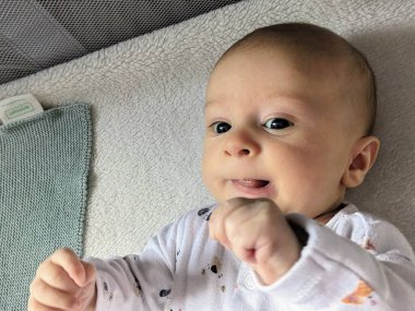 Üç aylık bir bebek, yumuşak battaniyeler ve hafif aydınlatmalarla çevrili, rahat bir beşiğinde uzanıyor, çocukluk döneminin masumiyetini ve sükunetini yakalıyor..