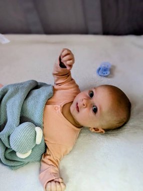 Üç aylık huzurlu bir bebek, yumuşak, doğal bir ışıkla kaplanmış, huzurlu bir beşiğinde yatar. Bu, erken çocukluğun yumuşak özelliklerini ön plana çıkarır.. 