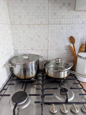 Standart mutfak tezgahına yerleştirilmiş iki kullanılmış metal tencerenin fotoğrafı. Sahne, ev yemeklerinde kullanılan temel yemek malzemelerinin altını çizerek, günlük yaşantısı olan bir mutfak ortamı yakalıyor..