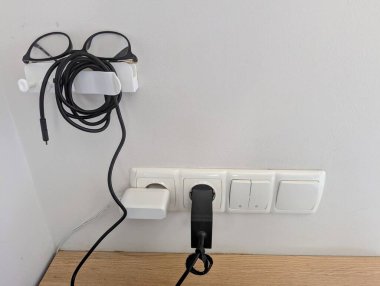 Elektronik aksesuarları düzenli tutmak için tasarlanmış parlak, beyaz bir tutucu. Tutucu düzgünce üzerine yerleştirilmiş bilgisayar gözlüklerine sahip ve yakınlardaki prizlere takılı bir dizüstü bilgisayar şarj aleti tutuyor.. 