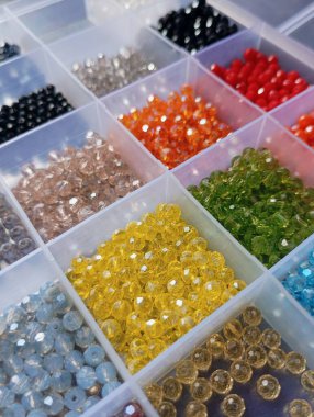 Plastik bölme kutusunda düzenlenmiş renkli parlak kristal boncuklar.