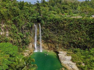 Ürkütücü bir tropikal şelale, yemyeşil ve kayalıklarla çevrili canlı bir turkuaz göle dökülüyor. Doğal güzellik, macera ve rahatlama temaları için ideal.