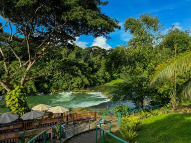 Bereketli tropik yeşilliklerle çevrili ve manzaralı bir şelaleye bakan, şemsiyeli, rahat bir açık hava kafesi olan nefes kesici bir nehir kenarı. Seyahat ve eko-turizm için mükemmel