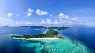 Kristal berraklığında turkuaz sular ve mercan resifleriyle çevrili tropikal bir adanın nefes kesici bir görüntüsü. Bereketli yeşillik, beyaz kumlu plajlar ve canlı deniz manzarası bir huzur hissi uyandırıyor.