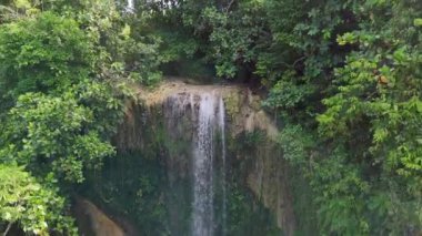 Yoğun, canlı yeşil yapraklarla çevrili, turkuaz bir havuza dökülen sakin bir tropikal şelalenin nefes kesici görüntüsü. Doğa, seyahat ve rahatlama temaları için mükemmel. Yüksek kalite 4k