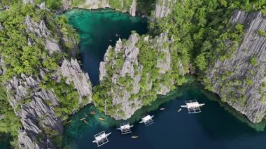 Kristal berraklığında turkuaz sular, yemyeşil çayırlar ve geleneksel teknelerle çevrili yüksek kireçtaşı kayalıkların çarpıcı hava manzarası. Huzurlu gölde kanolar ve küçük bir rıhtım bulunuyor.