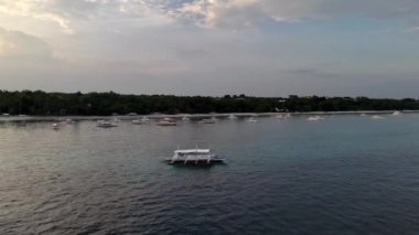 Sakin sularda geleneksel bir balıkçı teknesinin bulunduğu huzurlu bir günbatımı sahnesi, kıyıya yakın başka teknelerle çevrili ve arka planda sakin bir tepe kıyısı bulunuyor. Yüksek kalite 4k görüntü