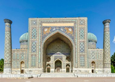 SamArkands Registan Meydanı 'ndaki tarihi medresenin etkileyici mimari manzarası. Ön cephe zarif mozaikler, turkuaz kubbeler ve karmaşık geometrik desenlerle süslenmiş.