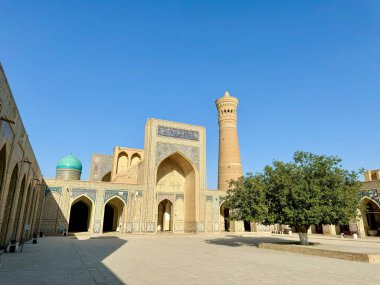 Bu resim, geniş bir avluda önemli bir minaresi olan muhteşem bir tarihi medreseyi tasvir ediyor. Çarpıcı İslami mimaride karmaşık mozaik döşemeler, canlı kubbeler ve kavisli