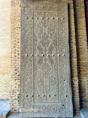 Close-up of a beautifully carved wooden door in Khiva, Uzbekistan, showcasing traditional Islamic artistry with detailed geometric and floral patterns. A testament to the craftsmanship and cultural clipart