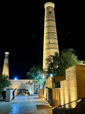 Özbekistan 'ın Khiva kentindeki İslam Khodja Minaresi' nin çarpıcı bir gece görüntüsü, karanlık gökyüzüne karşı parlak bir şekilde aydınlatılmış, karmaşık tuğla ve eşsiz mimarisini vurguluyor..
