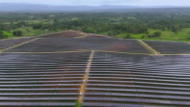 Geniş bir güneş enerjisi santrali, çevre yeşilliğin doğal güzelliğiyle modern yenilenebilir enerji altyapısını kusursuz bir şekilde harmanlayarak araziye yayılıyor. Özenle dizilmiş güneş.