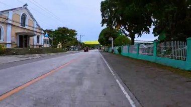 İçinde çan kulesi, yaya geçidi ve yemyeşil otlaklar olan tarihi bir kilisenin bulunduğu sessiz küçük bir kasaba caddesi. Sahne, klasik mimarisi ve kuyusu olan huzurlu bir yerel atmosfer yakalıyor.