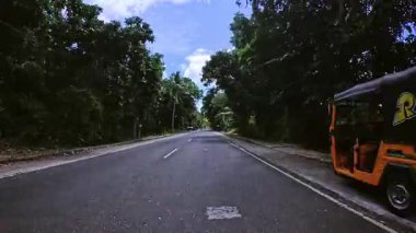 Huzurlu kırsal bir yol, yemyeşil bitki örtüsüyle çevrili olan mesafeye uzanıyor. Park halindeki beyaz arabalı küçük bir ev yol kenarında duruyor ve yerel hayata biraz renk katıyor. Asfalt yüzeyi