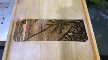 Bir lazer oyma makinesi ahşap bir yüzeye ayrıntılı bir palmiye ağacı dizaynı çizer. Hassas ve karmaşık süreç, el yapımı ve kişiselleştirmede kullanılan modern teknolojiyi sergiliyor. Bu görüntü...