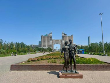 Geleneksel giyinmiş bir Kazak çiftin, manzaralı bir park alanına yerleştirilmiş bronz heykeli. Arkalarında etkileyici KazMunaygaz karargahı duruyor.