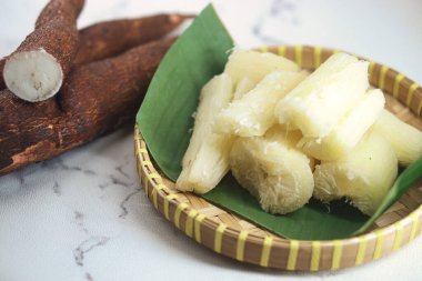 Muz yaprağında servis edilen taze kaynamış kaju parçaları, yanında da bütün kaju kökleri sergilenen dokuma bir bambu sepetinde. Doğal elementlerle geleneksel mutfak hazırlığının mükemmel bir temsili.