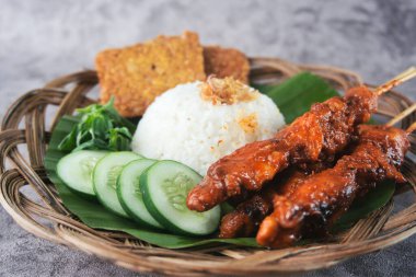 Geleneksel Endonezya mutfağının sunumunda satay şişler, buğulanmış pirinç, salatalık dilimleri, tempeh ve muz yaprağı astarlı taze sebzeler var.