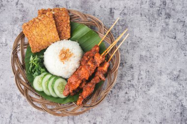Geleneksel Endonezya yemeği tavuklu satay şiş, beyaz pirinç, tempeh ve hasır bir tabakta doğal bir yaprakla süslenmiş salatalık ile servis edilir.