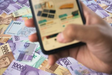 Banknotların yayılması, çevrimiçi para yönetimi, finans teknolojisi ve dijital finansal işlemlerin erişilebilirliğini sembolize eden finansal içeriklere el gezen bir akıllı telefonun yakın plan görüntüsü
