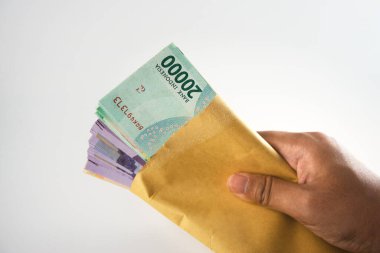 Endonezya 'nın 20,000 Rupia banknotuyla dolu kahverengi bir zarfı tutan bir el resmi, zenginliği, finansmanı veya hediye parasını sembolize ediyor. Kompozisyon para birimiyle ilgili temaları profesyonel bir tarzda vurgular