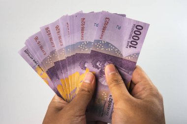Elleri sıkıca kavrama ve bir avuç Endonezya rupia para banknotlarını yelpazeleme, zenginlik ve finansal temaları vurgulama, tarafsız bir arka plan sağlama karşı