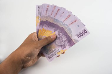 10 bin Endonezya rupia banknotundan oluşan bir desteyi sunan bir elin yakın çekimi. Düz beyaz arka plan kompozisyonu vurguluyor. Finansal ve para birimiyle ilgili konular için mükemmel