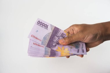 10 bin Endonezya rupia banknotundan oluşan bir desteyi sunan bir elin yakın çekimi. Düz beyaz arka plan kompozisyonu vurguluyor. Finansal ve para birimiyle ilgili konular için mükemmel
