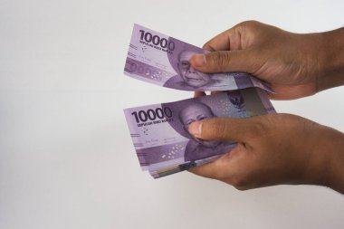 Yakın plan görüntü, Endonezya banknotlarının tutulduğunu ve sade bir arkaplanda iki elle değiş tokuş edildiğini gösteriyor.