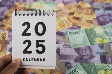 An arrangement featuring a 2025 calendar placed among multiple Indonesian rupiah banknotes. Highlighting themes of planning, finance, budgeting, and Indonesian currency, the composition reflects economic preparation for the year 2025 clipart