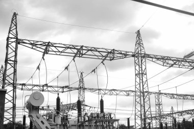 Black and white image of an intricate electrical power station network, showcasing various components and overhanging transmission lines set against a cloudy sky clipart